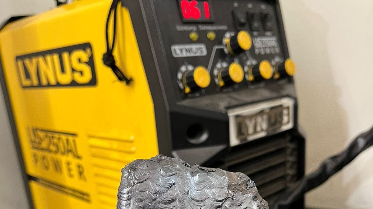 Máquina de solda industrial em bancada com corpo de prova soldado ao lado