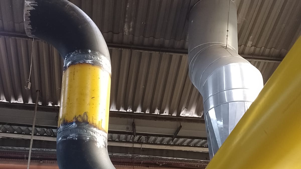 Tubulações industriais instaladas no teto de uma fábrica, com linhas pintadas e conexões soldadas